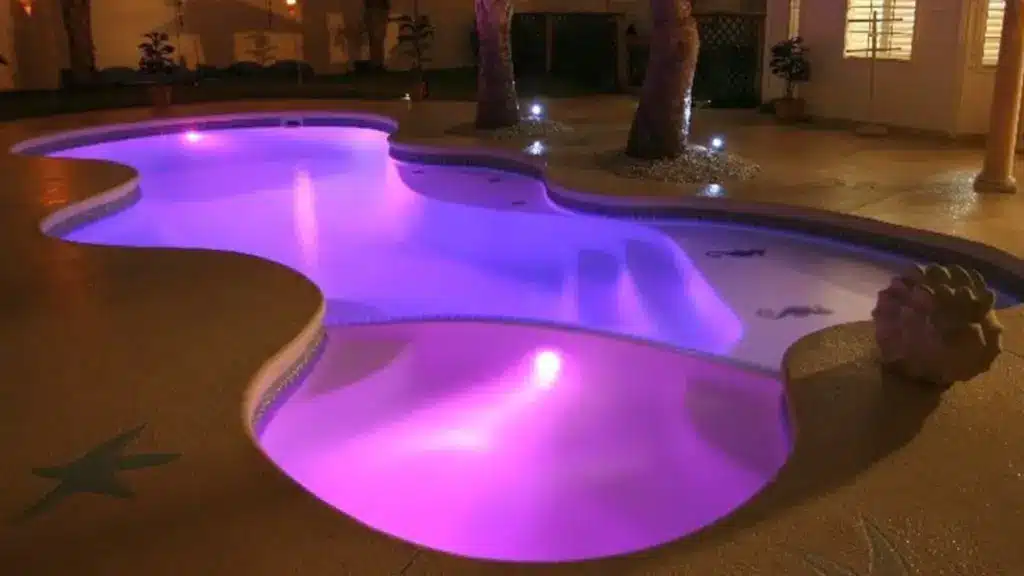 Freeform custom pool with seahorse mosaic tiles and purple underwater lighting.