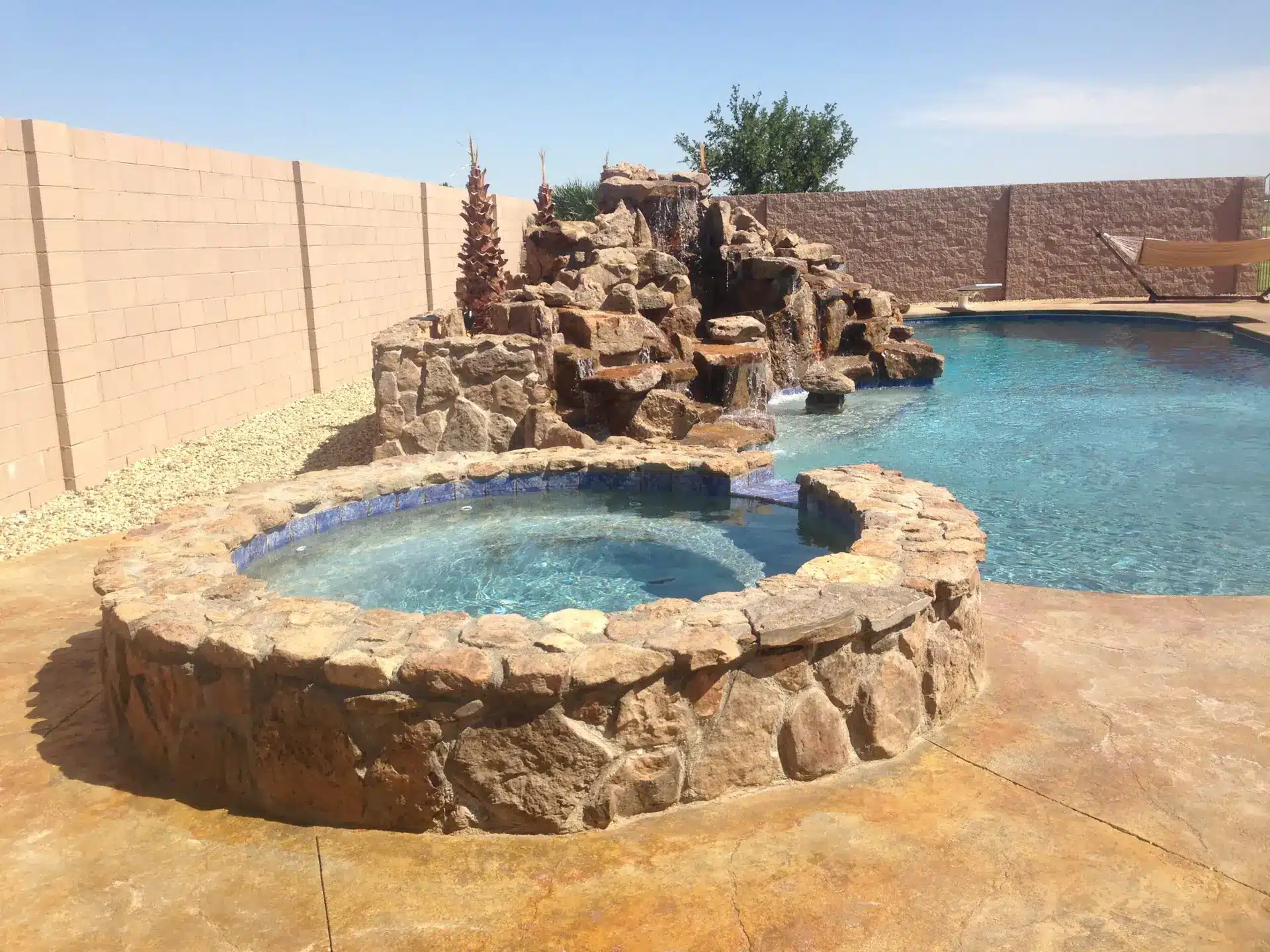Raised flagstone spa spilling into custom gunite pool with multi-tiered rock waterfall in Rio Rancho.