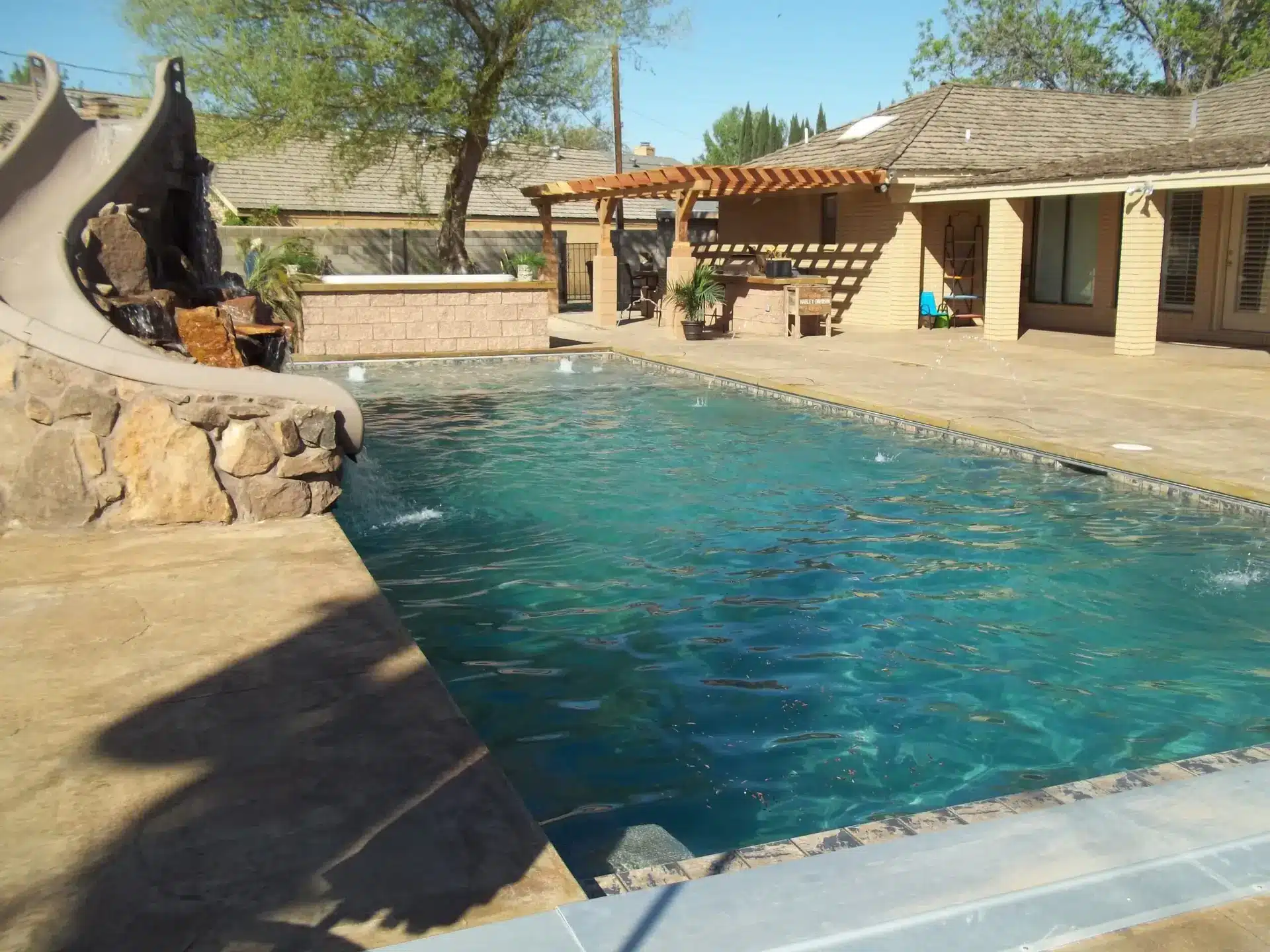 Custom pool with rock slide, sheer descent water feature, and timber pergola in Albuquerque backyard.