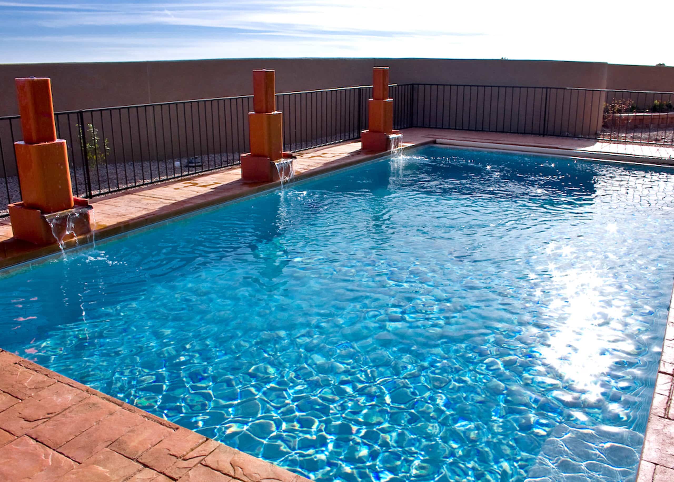 Custom pool with terracotta-colored column water features and reddish stamped concrete decking.